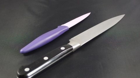 Zwei Messer liegen auf einer schwarzen Unterlage. Das scharfe Messer hat einen schwarzen Griff, das unscharfe einen lila Griff.