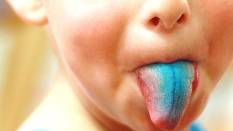 Ein Kind mit blauer Zunge zeigt den Effekt nach dem Essen von Waldheidelbeeren in einem hellen, unscharfen Hintergrund.
