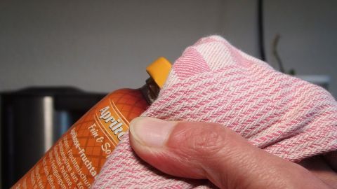 Eine Hand hält ein Fläschchen mit einem Schraubdeckel, während ein Tuch den Deckel fest umschließt, um ihn ohne Verletzungen zu öffnen.