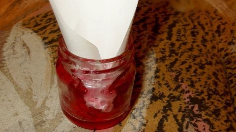 Ein Glas mit Marmelade steht auf einem Tisch, während ein Papiertrichter es kreativ als Fliegenfalle nutzt.