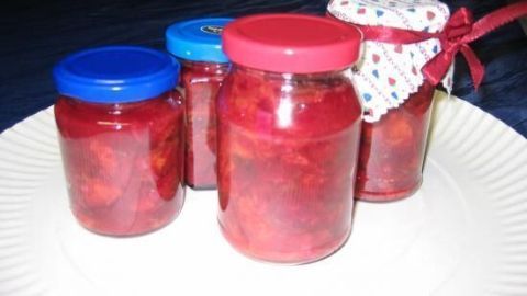 Gläser mit Pflaumen-Chutney stehen auf einem weißen Teller, mit verschiedenen bunten Deckeln, teils mit Stoff umhüllt.