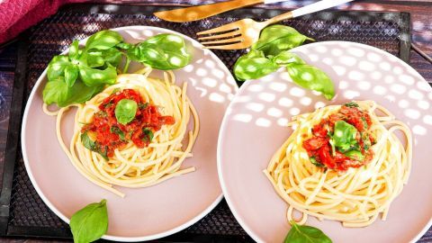 Spaghetti mit Tomatensauce und frischem Basilikum auf Tellern, gemütlich serviert auf einem Tisch.