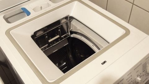 Eine geöffnete Waschmaschine zeigt die Trommel. Der Kontext ist ein Raum mit Fliesen, kein Text sichtbar.