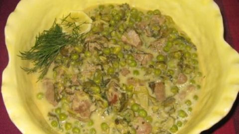 In einer gelben Schale liegt ein grünes Lammragout mit Erbsen und Kräutern, umgeben von einer festlichen Tischdecke.