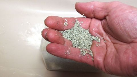Eine Hand zeigt Sand für ein Hände-Peeling, während sie über einen neutralen, hellen Hintergrund gehalten wird.