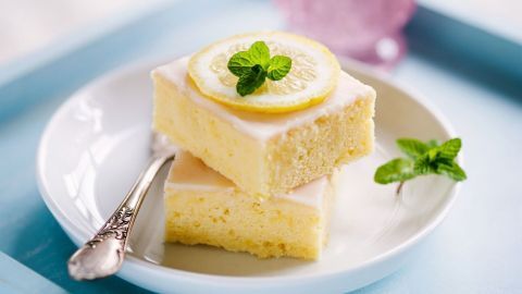 Ein saftiger Brausekuchen mit einer Zitronenscheibe und frischer Minze liegt auf einem weißen Teller, umgeben von einer pastellfarbenen Umgebung.
