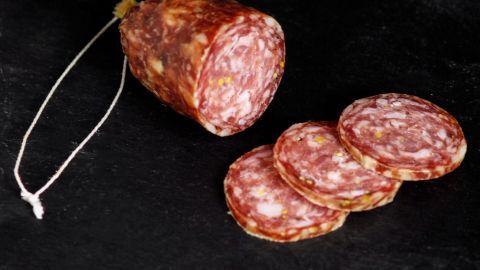 Wurstabschnitte liegen neben einer Wurst, die am Ende angeschnitten ist, auf einer dunklen Unterlage.