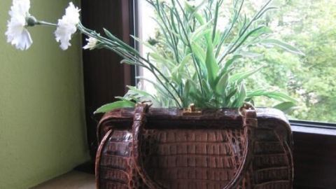 Eine alte Handtasche steht auf der Fensterbank und wird als Blumenvasen-Dekoration mit weißen Blumen genutzt.