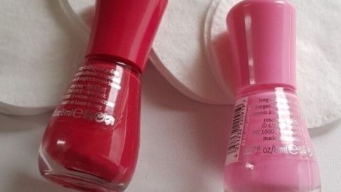 Zwei Nagellackfläschchen, rot und pink, liegen neben Wattepads. Sie können zum Entfernen von Nagellack verwendet werden.