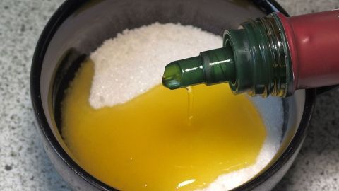 Eine Schüssel enthält Zucker und Olivenöl, während das Öl langsam eingegossen wird, um ein Körperpeeling zu erstellen.