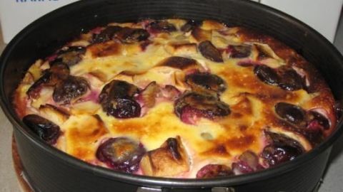 Ein Obstkuchen mit verschiedenen Früchten ist im Backring zu sehen, umgeben von Packungen für Zucker und Kakao.
