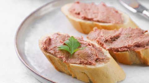 Auf einer weißen Platte liegen drei Brotscheiben mit geflügelleberwurst, garniert mit einem Blatt Petersilie.