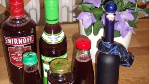 Eine Gruppe von Flaschen mit verschiedenen Likören und Säften steht auf einem Holztisch, umgeben von lila Blumen.