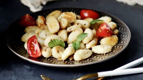 Gnocchi liegen auf einem schönen Teller, garniert mit frischen Tomaten und Minze in einer modernen Essumgebung.