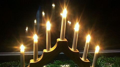 Ein dekorativer Kerzenständer mit brennenden Kerzen leuchtet in der Dunkelheit, umgeben von grünen Tannenzweigen für Weihnachten.