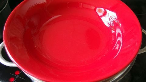 Ein roter Teller wird über einem Dampfgarer erhitzt, um ihn ohne Warmhalteplatte vorzuwärmen.