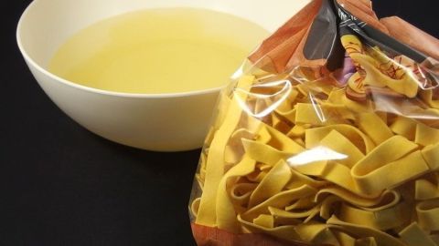 Eine Schüssel mit gesammeltem Kochwasser steht neben einer offenen Packung frischer Nudeln, bereit zur Wiederverwendung.