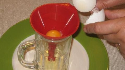 Ein roter Trichter trennt das Ei, während eine Hand ein Ei über ein Glas hält. Der Hintergrund ist ein gedeckter Tisch.