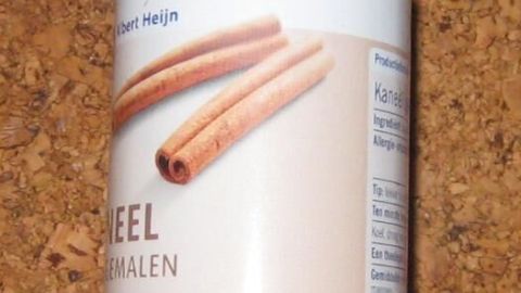 Ein Metallgewürzstreuer steht auf einer Holzoberfläche, bereit, Gewürze zu streuen, mit Gummiband zur Verschlussicherung.