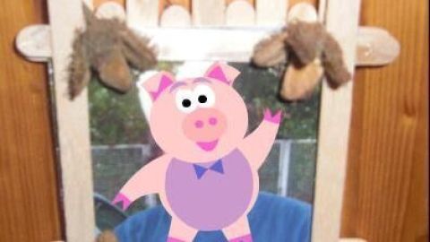 Ein Rahmen aus Holzstäbchen hält ein buntes Bild eines lachenden Schweins, mit verzierter Unterkante und Aufhängung.