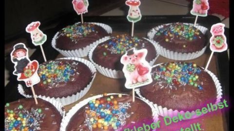 Sechs dekorierte Muffins stehen auf einem Tablett, verziert mit buntem Streusel und witzigen Spitzen.