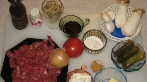 Auf einem Tisch liegen Zutaten für Rindfleisch Geschnetzeltes: geschnittenes Rindfleisch, Gemüse und Gewürze.