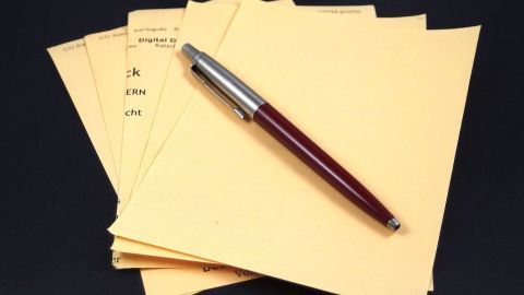 Staples of gelbes Papier liegen gestapelt, während ein Schreibstift daneben liegt, bereit zum Notieren von Tipps zum Papier sparen.