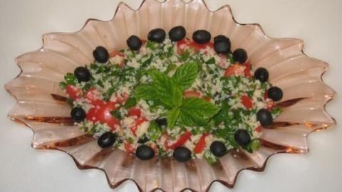 Tabouleh-Salat ruht in einer dekorativen Schale, garniert mit Oliven und Minzblättern, umgeben von einem weißen Hintergrund.