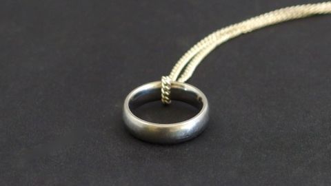 Ein alter Ring hängt an einer Kette und wird als Anhänger getragen, vor einem schwarzen Hintergrund.