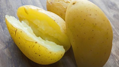 Gekochte Pellkartoffeln liegen auf einem Holztisch, eine aufgeschnitten und dampfend, bereit zum Servieren.