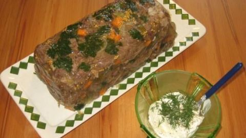 Ein länglicher, gelierter Tafelspitzsülze liegt dekorativ auf einer Platte, daneben ein Schälchen mit Kräuterquark als Beilage.