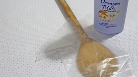Eine Holzkelle liegt auf einer durchsichtigen Folie neben einer Flasche mit Lotion für die Rückenpflege.