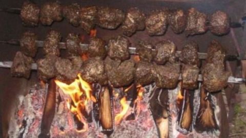 Mutzbraten dreht sich über offenem Feuer, umgeben von glühender Kohle, in einem rustikalen Grill-Setup.