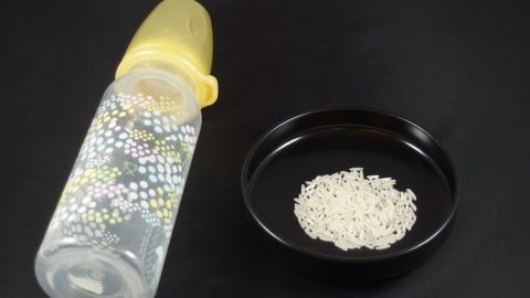Ein Babyfläschchen steht neben einer Schale mit ungekochtem Reis, bereit zum Reinigen mit Reis als Hausmittel.