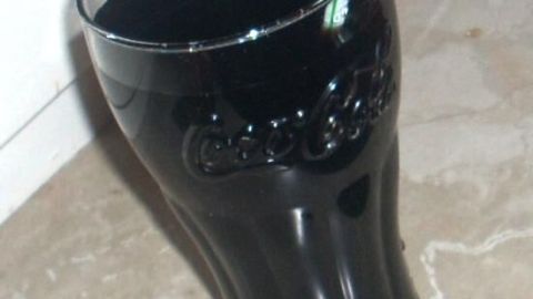 Ein Glas Cola steht auf einer marmorartigen Oberfläche. Ein Strohhalm ist darin platziert, um die dunkle Flüssigkeit zu trinken.