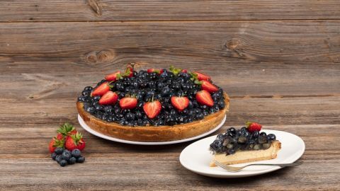 Ein Blaubeerkäsekuchen mit frischen Erdbeeren, angerichtet auf einem Holzuntergrund, wartet auf eine köstliche Verkostung.