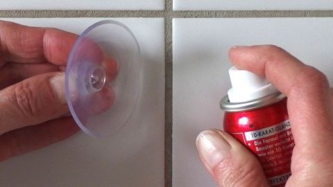 Eine Hand hält einen Saugnapf, während die andere ein Spray imitat mit Haarspray anwendet, um den Saugnapf sicher zu befestigen.