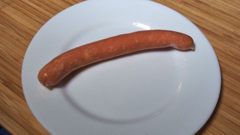 Ein Würstchen liegt auf einem weißen Teller und bleibt ganz, während es auf einer Holzoberfläche präsentiert wird.