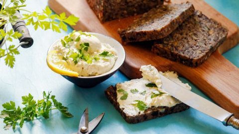Ein Brotaufstrich aus Petersilie wird auf dunklem Brot präsentiert, umgeben von frischen Kräutern und Werkzeugen.