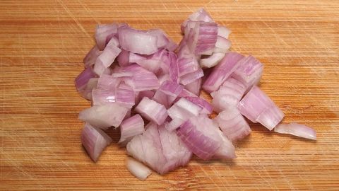 Auf einem Holzbrett liegen frisch gehackte Zwiebeln, die für das Kochen vorbereitet sind und einen intensiven Duft verbreiten.