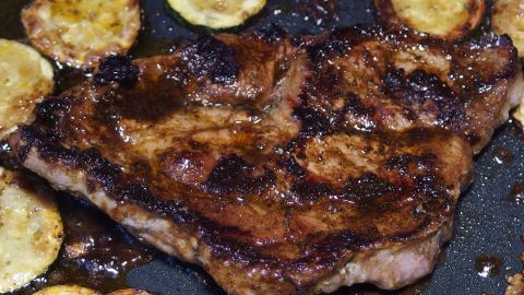 Ein saftiges Stück Fleisch brutzelt in einer Pfanne, umgeben von goldbraun gebratenen Zucchinischeiben.