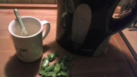 Eine Tasse steht neben einem Wasserkocher, während grüne Hustenbonbons auf der Holzoberfläche liegen, bereit zur Verwendung.