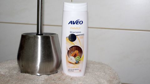 Eine Klobürste steht neben einer Flasche Shampoo auf einer hellen, gefliesten Oberfläche in einem Badezimmer.