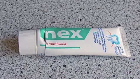 Vermeintlich leere Zahnpastatuben oder Kosmetika restlos aufbrauchen. Eine Zahnpasta-Tube liegt auf einer grauen Oberfläche, bereit zum Benutzen, um die Zähne zu reinigen und zu pflegen.