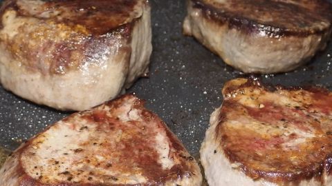 Saftige Steaks braten in einer Pfanne, goldbraun und knusprig, auf einem dunklen Hintergrund.