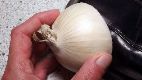 Ein Mensch hält eine halbierte Zwiebel, die auf einem schwarzen Lackschuh liegt, um diesen zu pflegen.