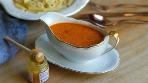 Eine elegante Soßenschüssel mit einer tomatigen Sauce steht auf einem Tisch, während daneben ein Teller Pasta serviert wird.