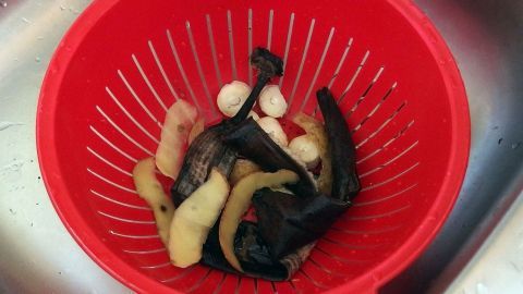 Rotes Sieb im Küchenspülbecken enthält Abfälle wie Obstschalen. Umgebung: Edelstahlspüle mit Wassertropfen.