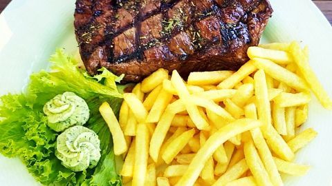 Ein saftiges Steak liegt auf einem Teller, umgeben von knusprigen Pommes und frischem Salat mit Kräuterbutter.