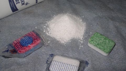 Spülmaschinenpulver liegt neben zwei verschiedenen Tabs auf einem grauen Untergrund, bereit für die Reinigung geschirr.